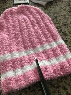 a pink and white knitted hat sitting on top of a counter next to a pair of scissors