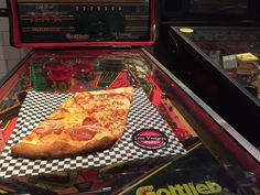 a slice of pizza sitting on top of a checkered paper towel in front of an arcade machine