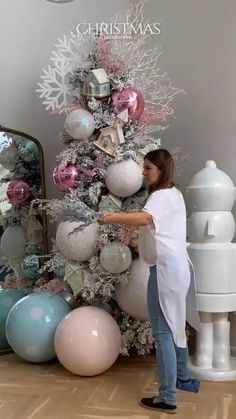 a woman standing in front of a christmas tree with balloons and ornaments on the top