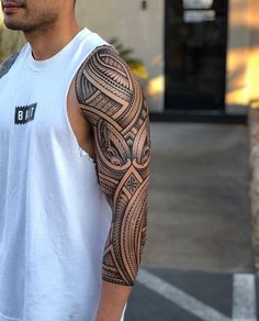 a man with a tattoo on his arm is standing in front of a building and looking off into the distance