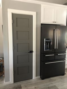 a black refrigerator freezer sitting in a kitchen next to a white wall and wooden floor