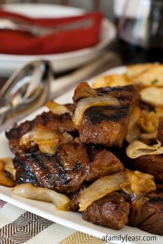 a white plate topped with meat and onions on top of a checkered table cloth