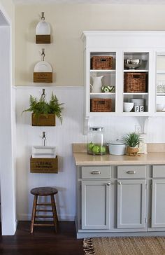 a kitchen with white cabinets and wooden floors, plants on the counter top and baskets hanging from the wall