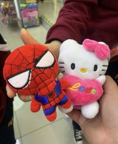 hello kitty and spiderman stuffed animals are being held by someone's hand in a store