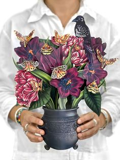 a woman holding a vase with flowers and butterflies in it's hands while wearing a white shirt