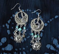 "Fun, flirty earrings with celestial charm that feature sun, half moon, and star charms swinging from filigree pendants with turquoise magnesite and glass bead accents! It's a super-cute pair of earrings to slip on to add that funky finishing touch to your outfits! And the're lightweight, too, so they're really comfortable to wear...no pulling as they swing! Choose your earwires...sterling silver or silver-plated! Sterling Silver/Silver-plated Earwires, Silver-plated Filigree Pendants 1\" round, Celestial Jewelry With Dangling Charms, Celestial Sun And Moon Dangle Jewelry, Celestial Star Jewelry For Festival, Celestial Star-shaped Festival Jewelry, Celestial Festival Star Jewelry, Whimsical Moon Charm Dangle Jewelry, Whimsical Dangle Moon Charm Jewelry, Whimsical Dangle Jewelry With Moon Charm, Celestial Metal Jewelry With Dangling Charms