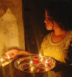 a woman holding a tray with lit candles in it and looking at the light coming from her hand