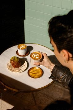 a woman sitting at a table with three cups of coffee and cookies in front of her