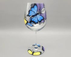 a wine glass with blue and yellow butterflies painted on the side, sitting in front of a gray background