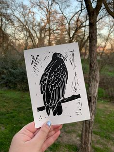 a person holding up a card with a bird on it in front of some trees