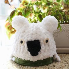 a white polar bear hat sitting on top of a counter next to a potted plant