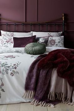 a bed with purple and white comforters, pillows and blankets on top of it