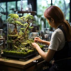 a woman is working on a bonsai tree in a glass case at a table