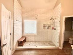 an empty bathroom with white tile walls and wood flooring, including a walk in shower