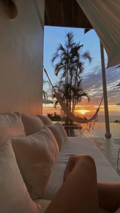 the sun is setting over an outdoor pool with white couches and palm trees in the background