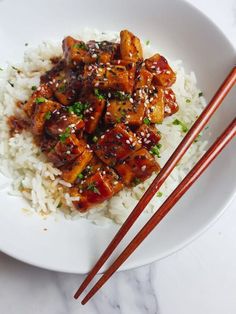 a white plate topped with rice and meat next to chopsticks on a table