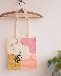 a tote bag hanging on a wooden hanger next to a potted plant