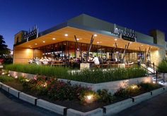 the outside of a restaurant at night with lights on and plants growing out of it