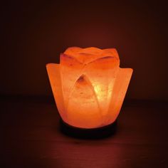 an orange himalayan stone lamp sitting on top of a wooden table in front of a dark background