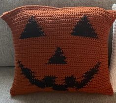 an orange crocheted pumpkin pillow sitting on top of a couch next to a white pillow