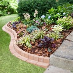 a garden with flowers and plants growing in the ground next to a brick planter