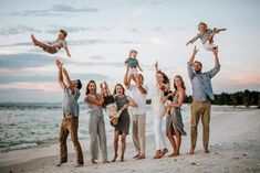 a group of people standing on top of a beach next to the ocean holding up babys