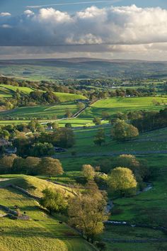 an aerial view of the countryside with trees and fields in the foreground, under a cloudy sky