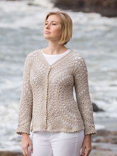 a woman standing on the beach wearing a sweater and white pants with her eyes closed