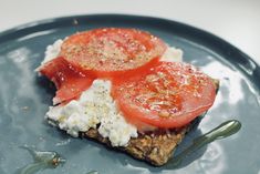 a piece of toast topped with tomatoes and cottage cheese on a blue plate next to a fork