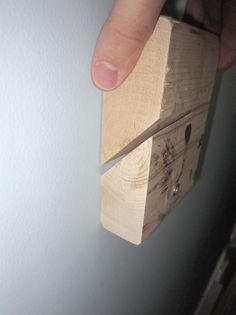 a person is holding a piece of wood in front of a wall mounted light switch