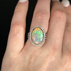 a woman's hand holding an opal and diamond ring