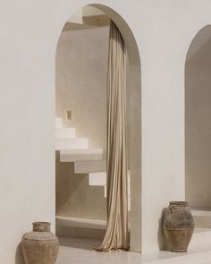 two vases sitting next to each other in front of a white wall with arches