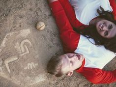 a man and woman laying on the ground next to each other with their faces drawn in sand