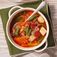 a bowl of soup with meat, vegetables and bread on a green napkin next to a spoon