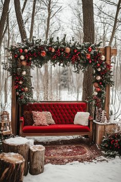 a red couch sitting in the middle of a forest with christmas decorations on top of it