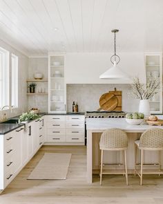 a kitchen with white cabinets and counter tops next to two stools in front of an island