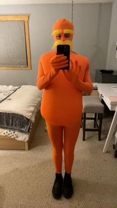 a woman in an orange costume taking a selfie with her cell phone while standing in a bedroom