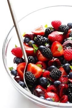 a bowl filled with berries and strawberries on top of a white table next to a spoon