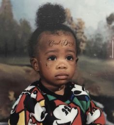 a young child with tattoos on her face and hair is sitting in front of a painting