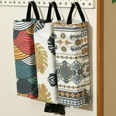 three bags hanging from hooks on a wall with decorative patterns and black handles in front of them