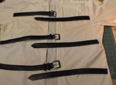 four pairs of black belts are laid out on a piece of white fabric, and the belt is attached to an unbuttonled jacket