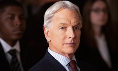 an older man in a suit and tie looking at the camera with other people behind him