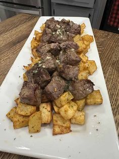 a white plate topped with meat and potatoes on top of a wooden table next to an oven