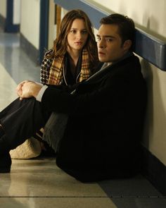 a man and woman sitting on the floor next to each other in front of a wall