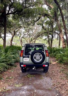 a car parked on the side of a dirt road in front of trees and bushes