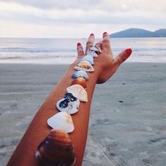 a woman's arm with seashells on it and the ocean in the background