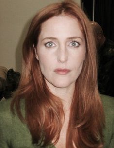 a woman with red hair and blue eyes is looking at the camera while wearing a green shirt