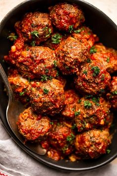 a pan filled with meatballs covered in marinara sauce and garnished with parsley