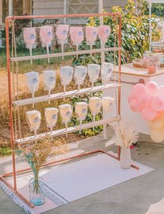 a table topped with lots of pink and white balloons next to a cake stand filled with wine glasses