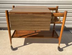 a wooden table with two chairs on it and a shelf under the top that is holding a magazine rack